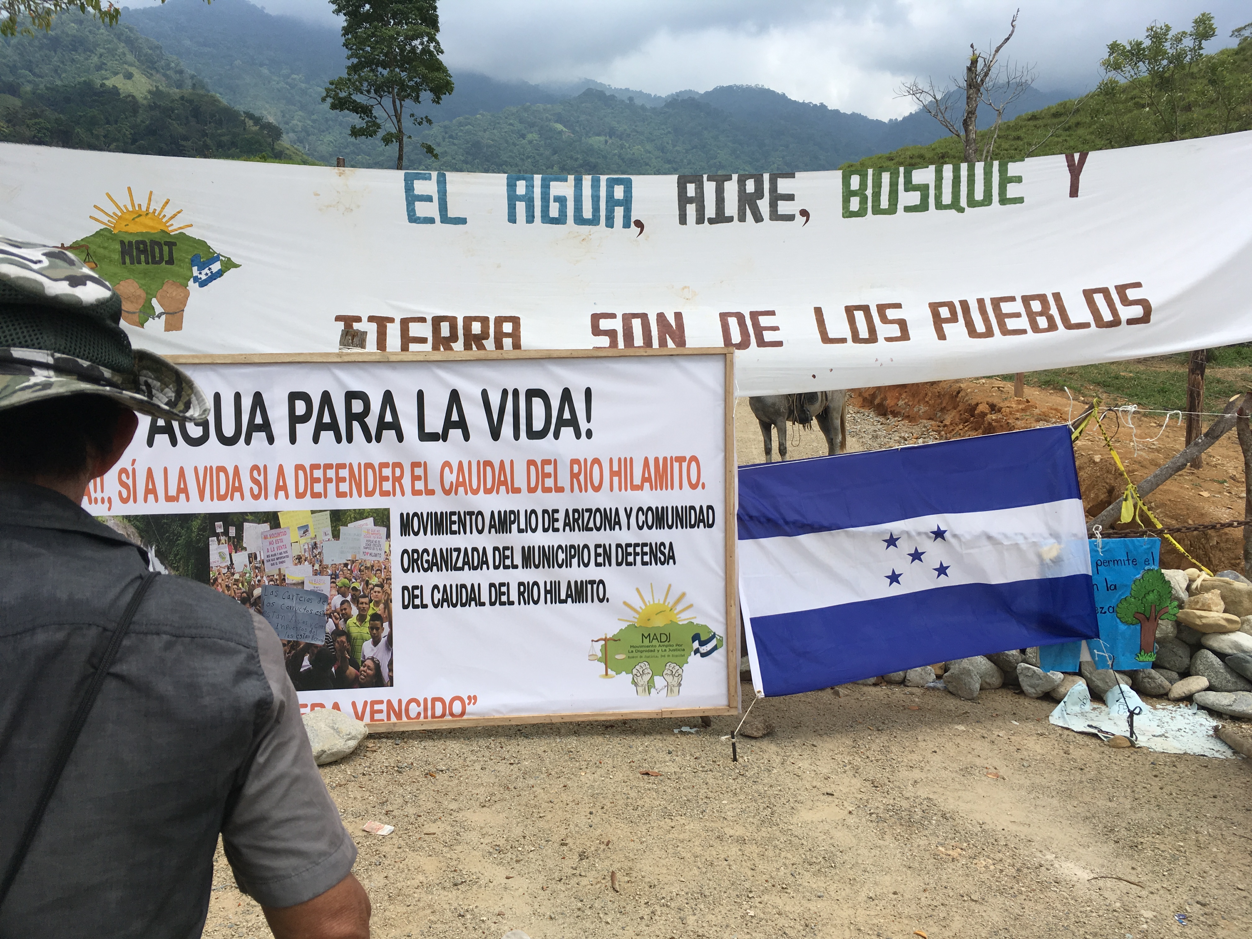 Picture is of a banner, sign, and Honduran flag that cover barbed wire and make up a barricade